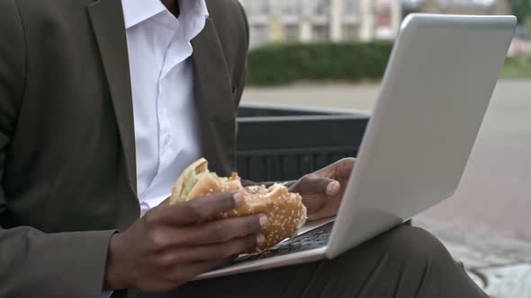 Closeup of Businessman Chewing Burger and Using Laptop Outdoors
