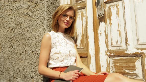 Gorgeous Woman Sitting by the Door and Leaning Against Wall with Book