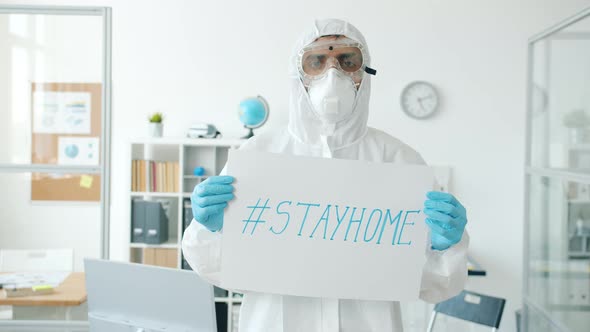 Portrait of Man in Quarantine Suit Standing in Empty Office with Stayhome Banner alt