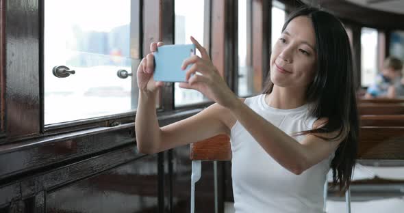 Woman taking photo on cellphone inside ferry at Hong Kong city 