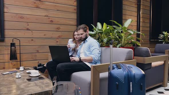 Attractive Young Modern Couple Sitting in Hotel Lobby and Looking at the Computer