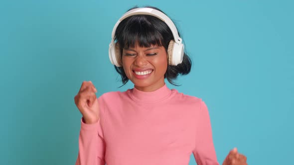 Young Woman Dances with Arms Raised with Great Songs in Headphones Blue Wall