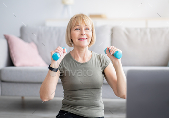 Online sports training at home. Attractive senior woman doing exercises with dumbbells near laptop / Photodune, Misc