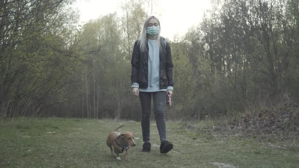 Young Blond Woman Walking with Dog on Sunset in Natural Parkland. Wide Shot of Owner and Pet