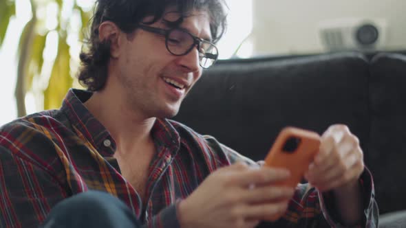 Laughing adult man in a plaid shirt texting by phone