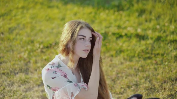 Portrait of Beautiful Longhaired Lady Sitting on Grass Among Sunny Nature