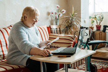 y for Seniors. Mature woman in glasses with Laptop and documents on the background of Rollator Mobility Walker for Seniors at home