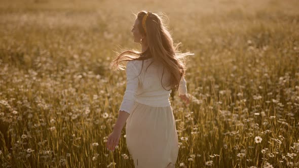 A Happy Woman is Running in Slow Motion Across Field with Camomiles at Sunset