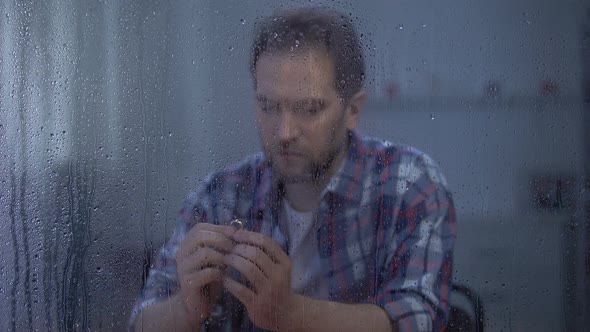 Upset Man Holding Engagement Ring on Rainy Day, Divorce Concept, Family Conflict