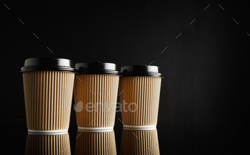 fee cups with black lids in a row on reflective black table against black wall