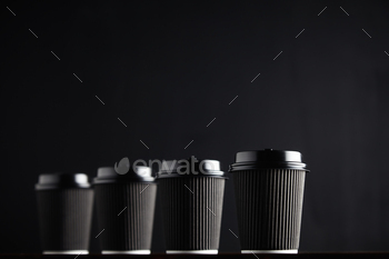 cardboard coffee cups with black lids on black table against black background