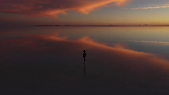 Silhouette of a man at Salar de Uyuni salt flat during sunset nightfall, orbital 360 drone shot, dar