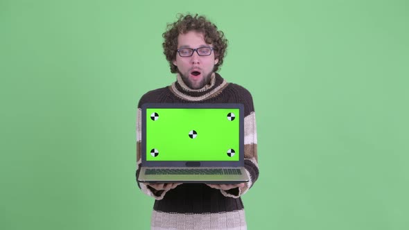 Happy Young Bearded Man Showing Laptop and Looking Surprised