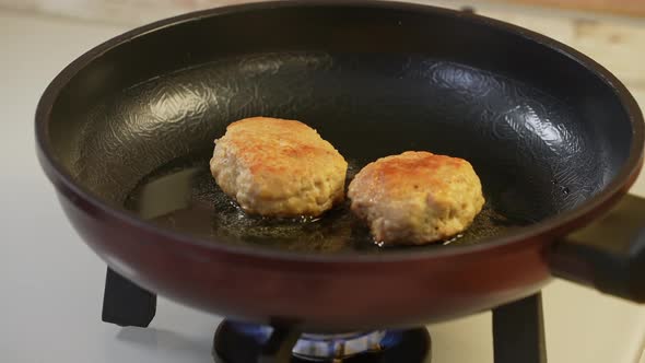 Two Chicken Cutlets are Fried in a Black Frying Pan in Olive Oil