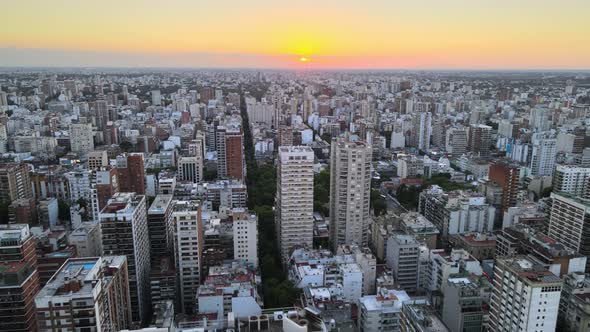 Dolly out flying over Belgrano neighborhood buildings at sunset with bright sun in horizon, Buenos A