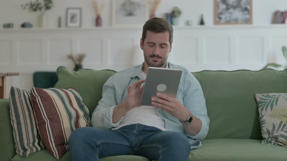 Young Man Having Loss on Tablet on Sofa