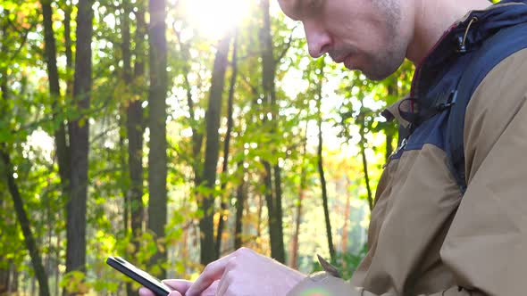 A Backpacker Works on a Smartphone in a Forest - Closeup From the Side