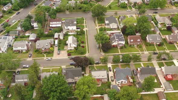 An aerial view over a suburban neighborhood on a cloudy day. The camera dolly in, tilt down then pan