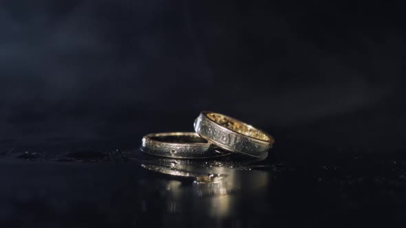 Wedding Rings on Dark Water Surface Shining with Light. Close Up Macro