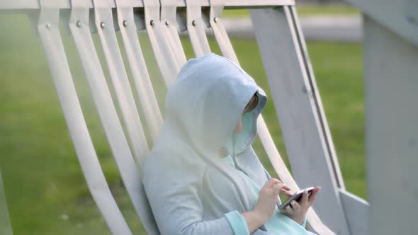 Sad Woman in the Hood Uses the Phone Outdoors in the Rest Area in the Evening Cinematic Shot