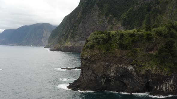Aerial is flying along the coast of Seixal and reveals a small waterfall, madeira