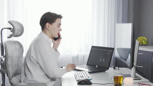 Female Entrepreneur Talking on Her Phone While Working on Two Computers