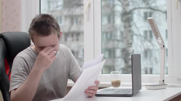 A young guy is reading documents and he is saddened, he is wearing a gray t-shirt