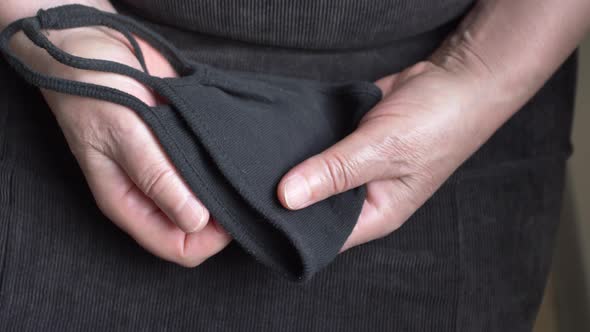 An Elderly Woman's Hands Holding the Medic Multi Use Mask All Wearing Is Black