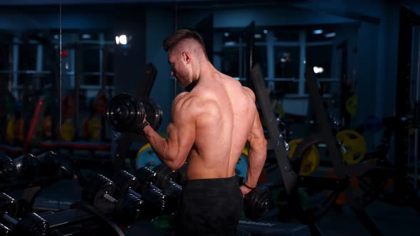 Fit young man lifting dumbbells doing workout at a gym.