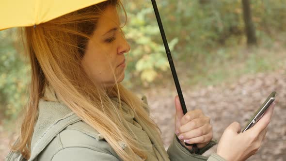 Blonde female outdoor using mobile phone while raining 4K 3840X2160 UltraHD footage - Blond woman wi