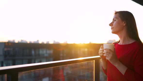 Woman with a Cup of Coffee Standing on the Balcony and Admire the Sunset