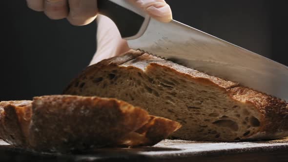 Person in Gloves Cuts Slice of Warm Bread on Wooden Board