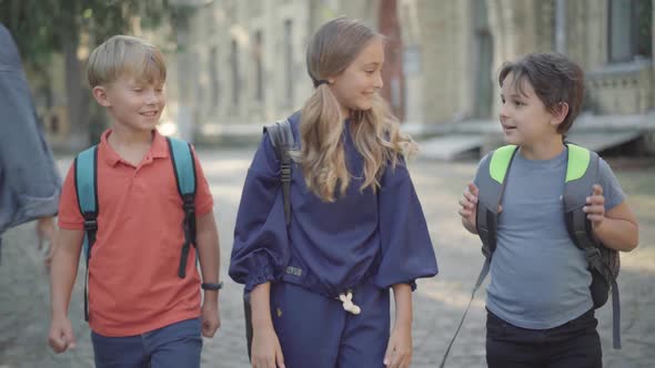 Portrait of Cute Excited Little Schoolgirl Walking with Classmates and Talking As High-school