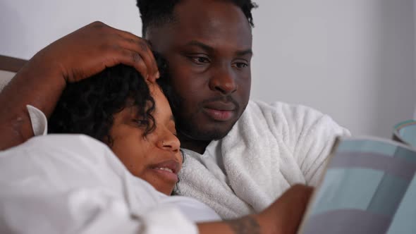 Closeup Portrait of Happy African American Couple Talking Smiling Reading Book Lying in Bed at Home