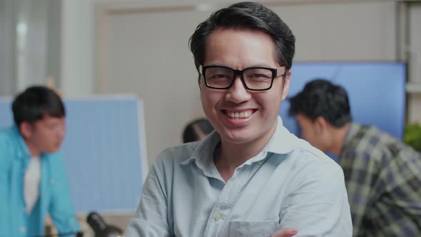 Close Up Of Smiling Asian Man Engineer Crossing His Arms To Camera While His Colleagues Working