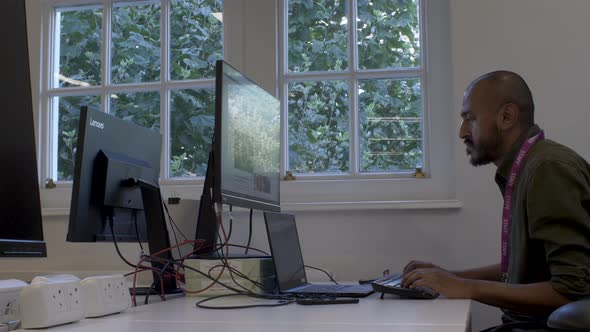 Modern Ethnic Minority Male Office Worker Typing At Desk. Side View, Static Shot, Low Angle