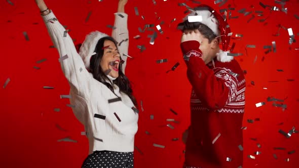 Excited Couple Santa Claus Hats Dancing, Having Fun, Rejoices Over Confetti Rain