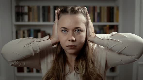 The Lady Is Sitting in Front of Bookshelf and Closes Her Ears with Both Hands