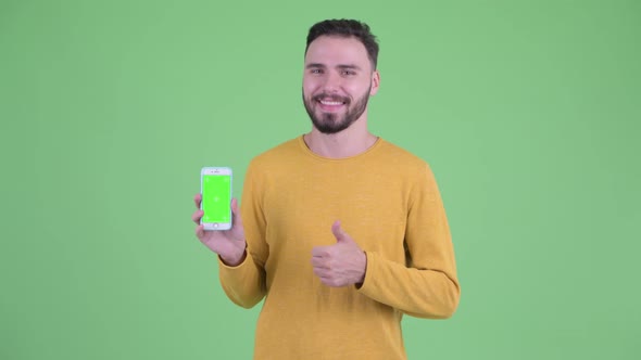 Happy Young Handsome Bearded Man Showing Phone and Giving Thumbs Up