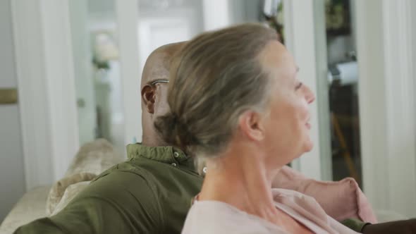 Happy senior diverse couple wearing shirts and watching tv in living room