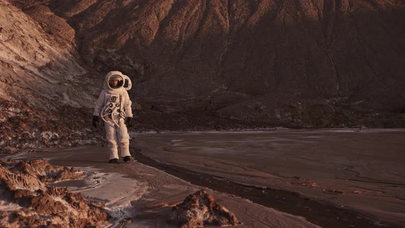 the Astronaut Walks Cautiously Along the Stream Raises His Hand