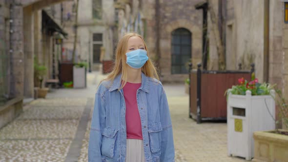 A Young Woman Wearing a Face Mask Walks Between Old European Buildings