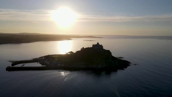 Aerial circling around St Michael Mount with coast in background at sunset, Cornwall