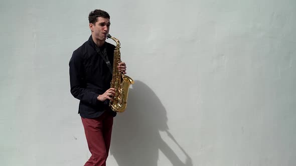 Street Musician Is Playing Saxophone at White Wall Background Outdoors, Performing Melody and Song