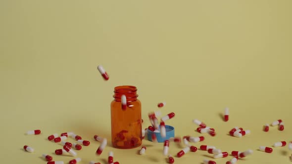 Slow motion wide shot of pills as they fall vertically towards an open pill bottle and lid. Some fal