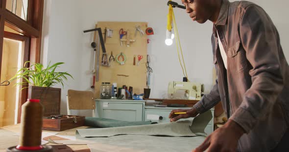 Focused african american craftsman preparing leather in leather workshop