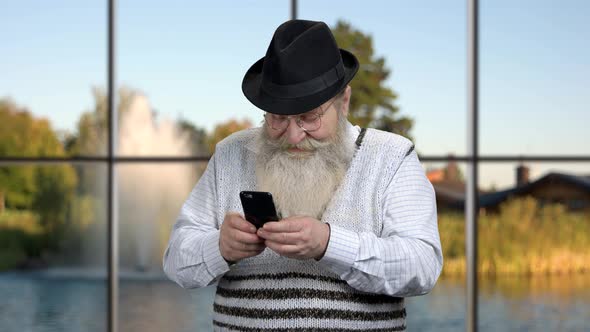 Funny Senior Man Using App on His Mobile Phone.