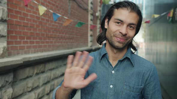 Smiling Mixed Race Guy Waving Hand Greeting Looking at Camera Outdoors with City in Background