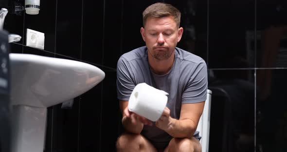 A Man with a Roll of Paper Sits on the Toilet