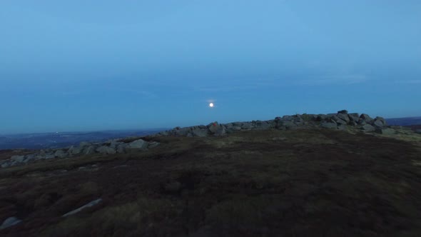 Aerial shot of men climbing boulders while bouldering at night under a full moon.